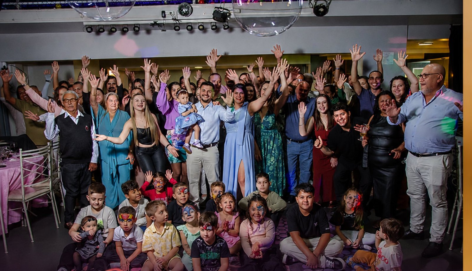 Famílias reunidas comemorando de mãos para o alto no salão iluminado da FesThay em Santa Maria