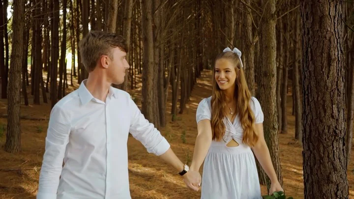 Casal de mãos dadas caminhando entre os troncos altos do bosque de pinheiros