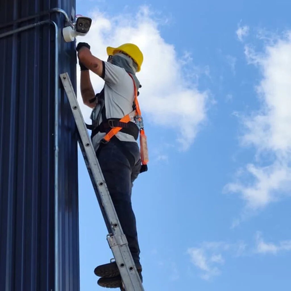 Técnico da PRS, de capacete e cinto de segurança, instalando uma câmera em altura
